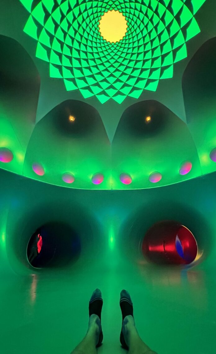 Green lighting fills a room with high ceilings, dotted with red and yellow lights. Architects of Air: Daedalum