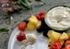 Easy Fruit Dip Berries and pineapple on a white plate with a bowl of creamy white fruit dip, and a little gold spoon with some of the dip on a plate
