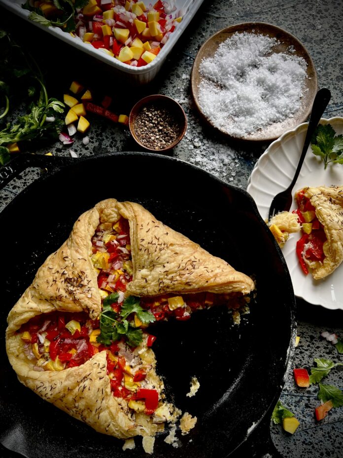 A summer veggie en croute, puff pastry filled with chopped vegetables in a cast iron skillet