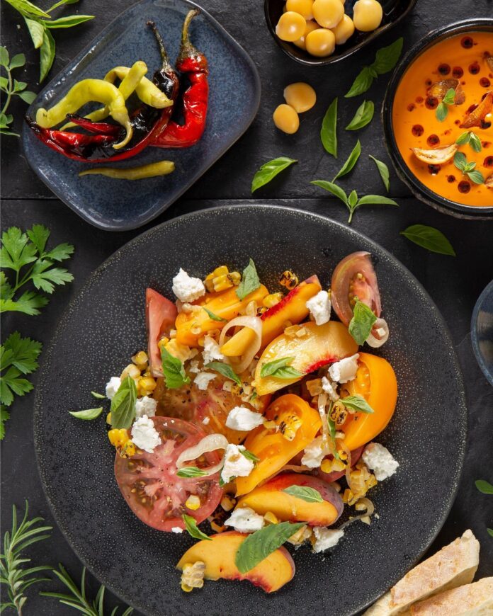 a colorful Tomato Peach Salad sits on a black plate