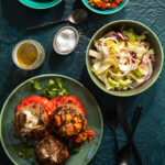 An aerial shot of Three Balkan Burgers sitting on a green plate. Off to the right side are bowls of toppings.