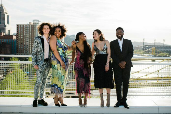 a diverse group of 5 people in cocktail attire on a rooftop overlooking the Allegheny River in Pittsburgh. Riverlife's 2023 Party at the Pier