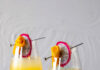 Rio Cocktail, Inspired by Duran Duran Two identical cocktails in iridescent wine glasses garnished with dragon fruit pinwheels and mango rolls made to look like roses.