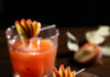 Sunrise, Sunburn, Sunset Cocktail, Inspired by Luke Bryan Two orange colored cocktails in rocks glasses with peach fan garnish and a dark background