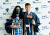 Lifelong Friends at PA Cyber Receive Full College Scholarships Two students dressed in graduation garb holing diplomas in front of a PA Cyber step and repeat