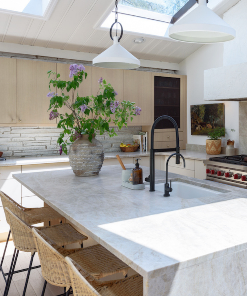 A kitchen island with white marble top and a vase with purple flowers on it too.