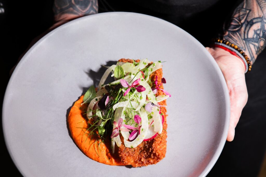 A round plate with an orange sauce and greens on top of it.