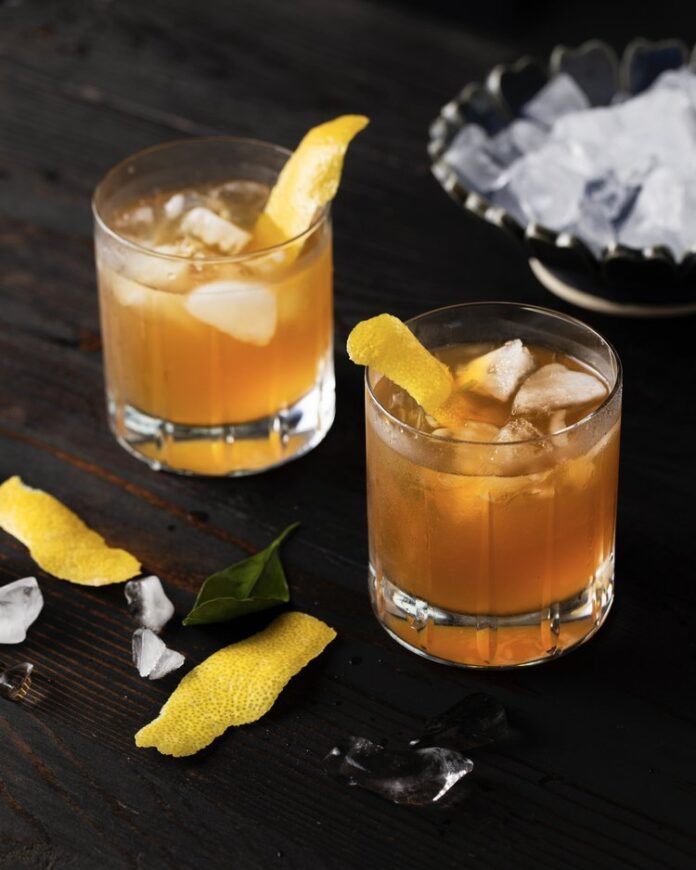 Game Day Cocktail 2 identical whisky cocktails in rocks glasses, garnished with lemon peel with a black background