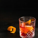 A light red cocktail in a rocks glass with an orange peel inside the glass. Negroni Con Alma Recipe