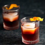 Two Espresso Negroni Cocktails in rocks glasses with an orange peel as garnish. Deep red in color. Espresso Negroni Cocktail Recipe