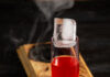 Coo Coo for Coconuts Negroni A cocktail red in color sits on a wooden board that is slightly burnt with smoke pouring out. Coo Coo for Coconuts Negroni