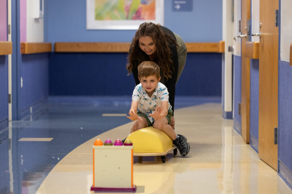 a women pushes a child on a toy with wheels at The Children's Institute
