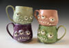 Pickled Aliens’ Handcrafted Pottery with a Halloween Twist Four monster-looking pottery mugs painted green, pink, purple, and grey.