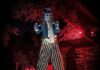 Get Scared with 10 Haunted Attractions Near Pittsburgh A clown in striped pants on stilts stands outside in front of red lights.