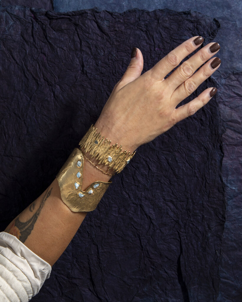 A women with painted nails shows off her arm adorned in gold and turquoise jewelry.