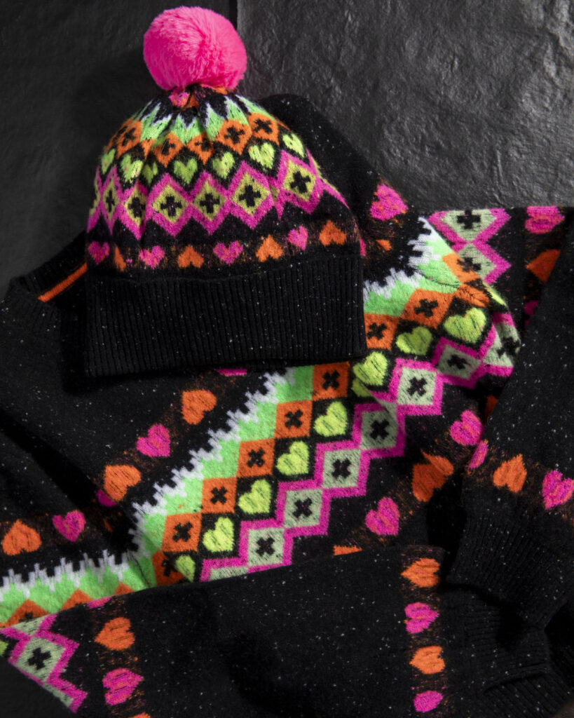 A colorful sweater and matching beanie with a pink pom on top.