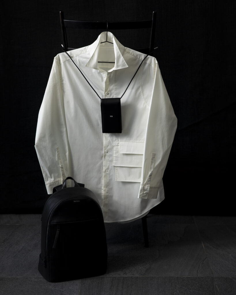 A white long sleeve button-up shirt styled on a chair with a black bag and phone holder.