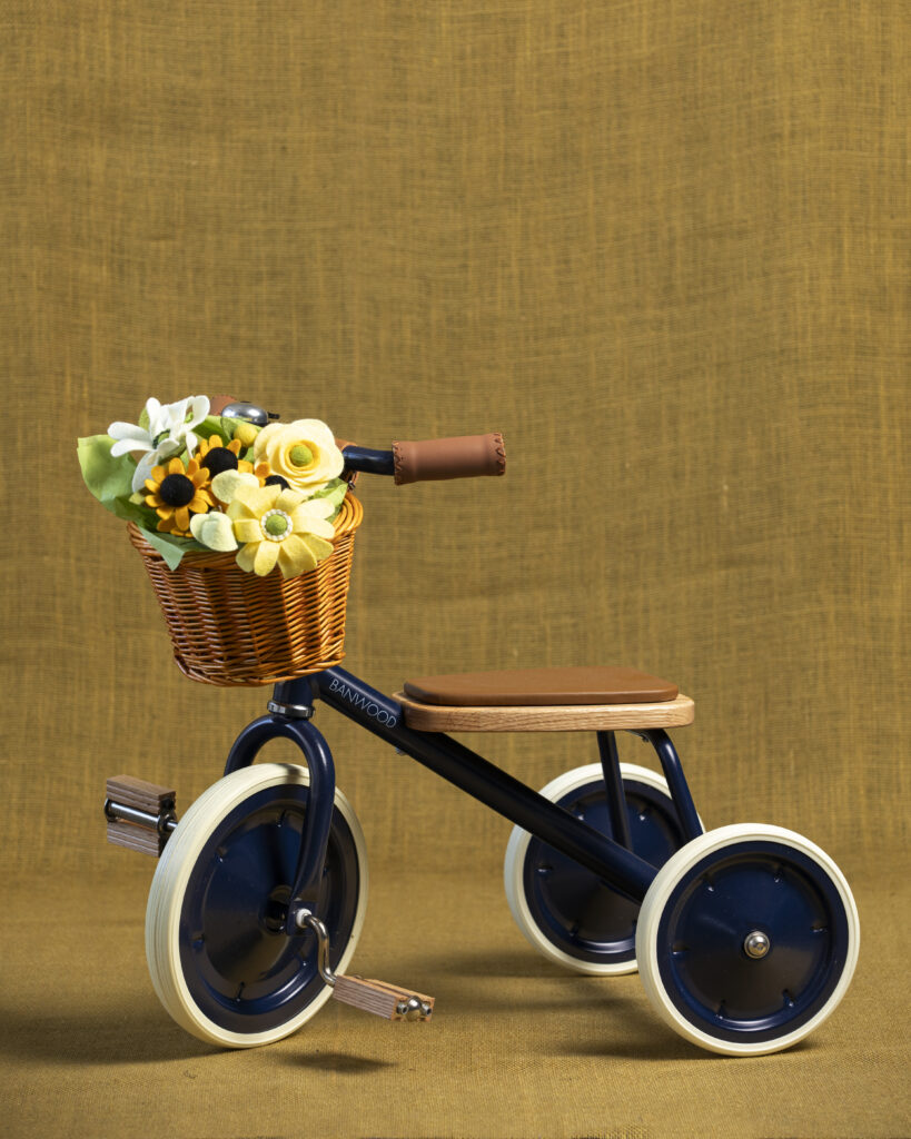 A small tricycle with black wheels and a small basket filled with flowers on the handle bars.
