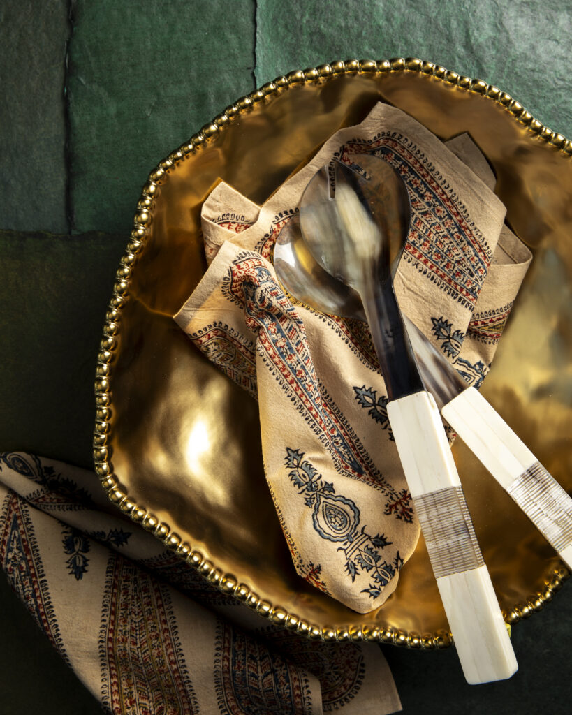 A golden serving bowl filled with utensils and a towel.