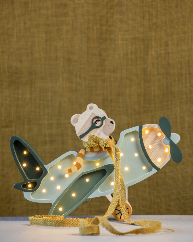 A bear flying an airplane lamp that lights up with small bulbs on the outside in front of a brown backdrop.