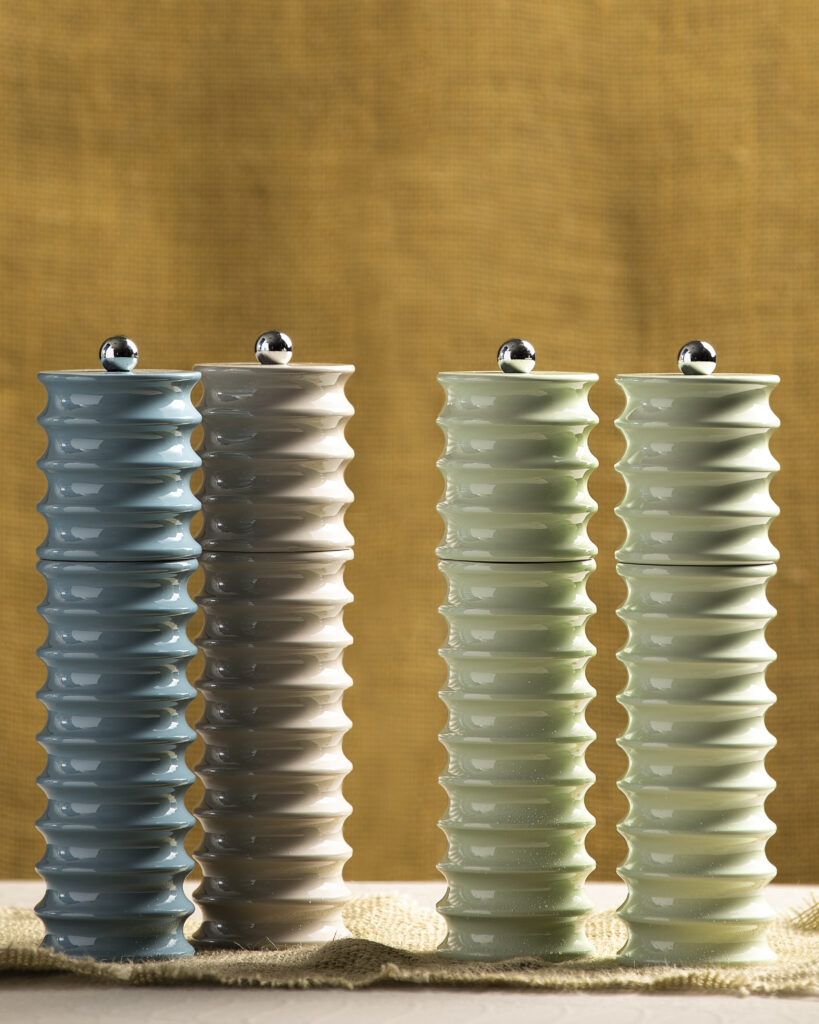 Green, blue, and brown spiraled pepper and salt grinders set on a tabletop.