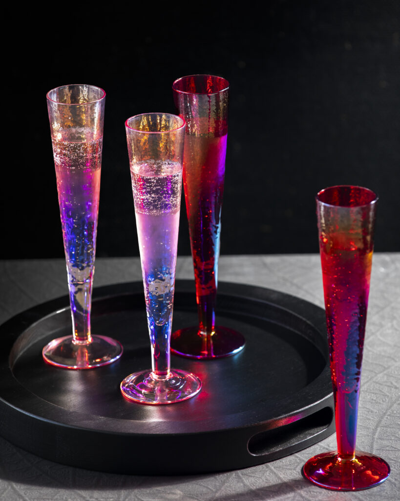 Colorful rainbow champagne flutes on a black tray.