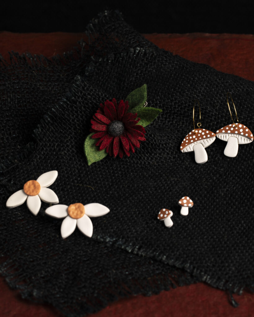 Different sets of flower and mushroom earrings laid out on a black background.