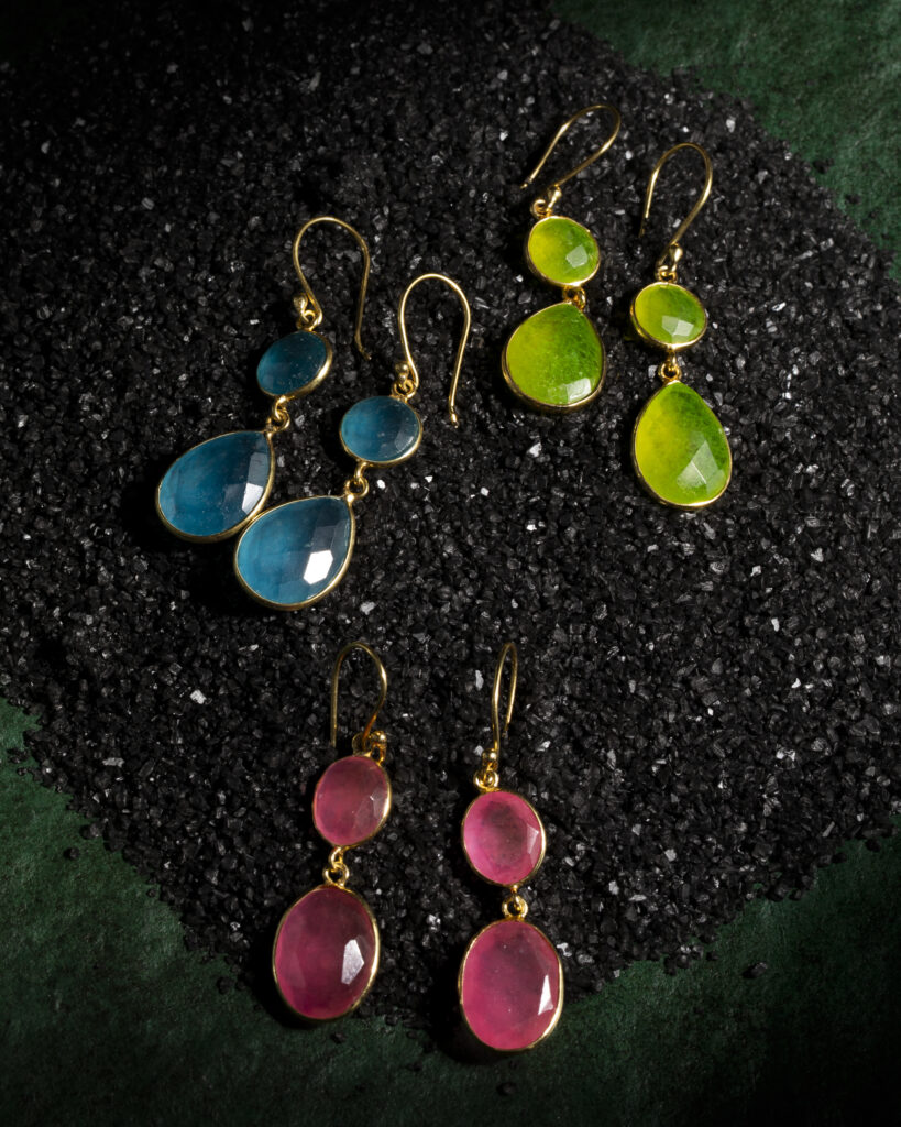 Three sets of colorful blue, pink, and green earrings on a black background.