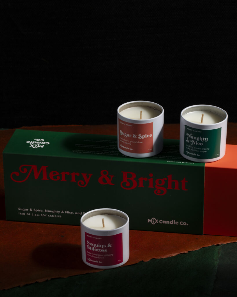 Three holiday candles sitting around a holiday-themed gift box.