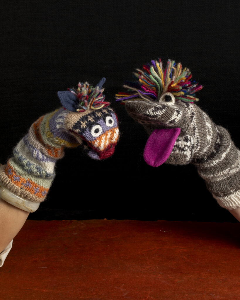 Two colorful sock puppets with pom pom hair on two different arms.