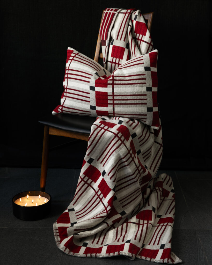 A red striped and blocked pattern on a blanket and purse modeled on a chair.