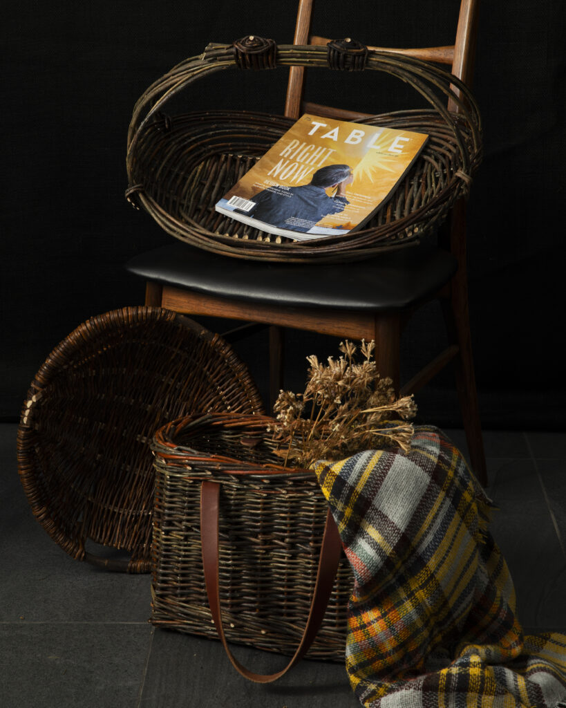 Wicker baskets filled with blankets and TABLE magazines on a chair.