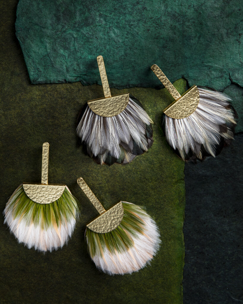 Two pairs of white feather earrings with a touch of color on a table backdrop.