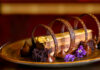 Coffee Costa Crunch A chocolate coffee crunch log surrounded by edible flowers, chocolate kisses, and four chocolate rings on a plate.