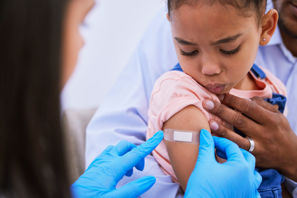 A doctor or nurse putting a bandaid on a child's arm after receiving a vaccine.
