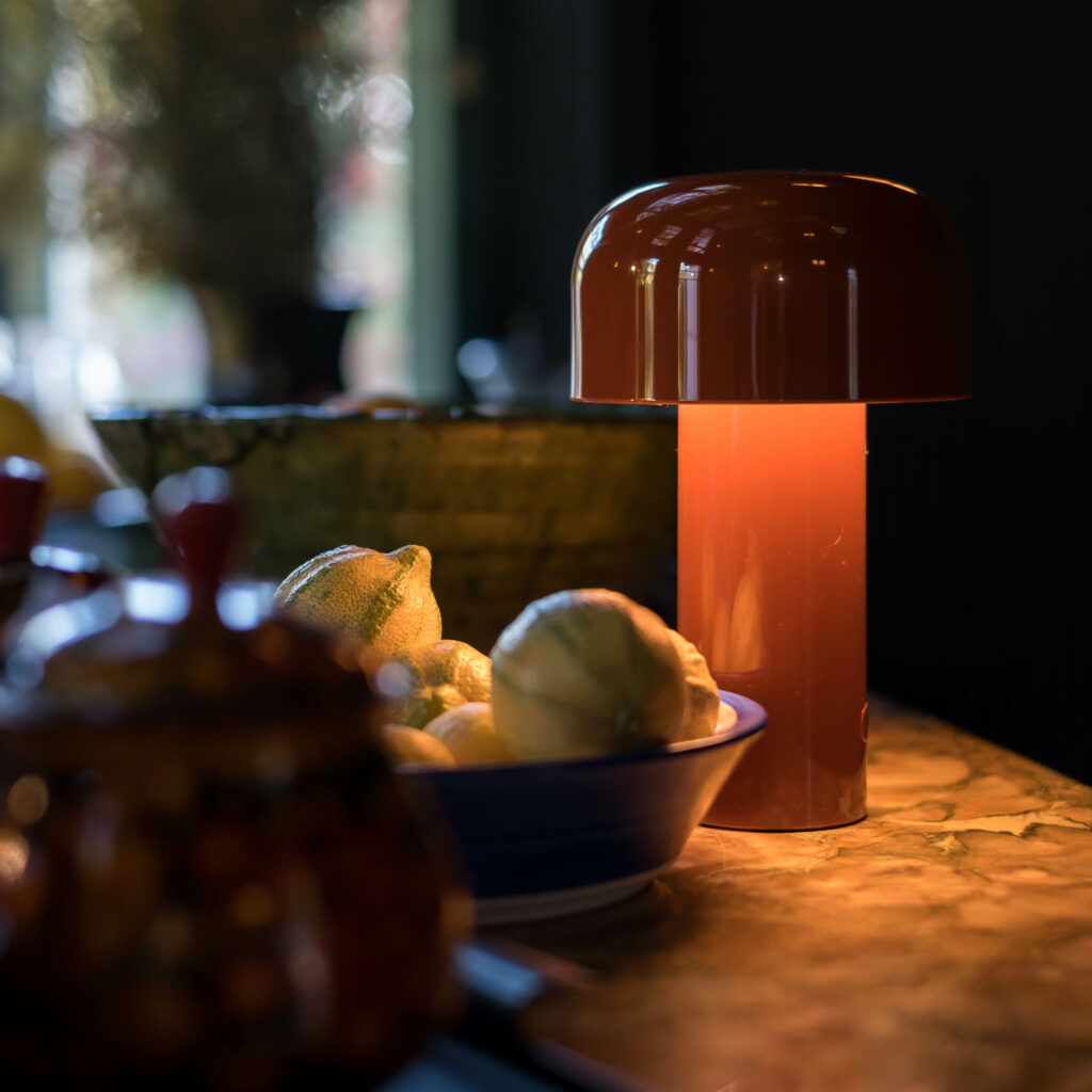 A lowly lit counter by a small lamp filled with fruits and bowls.