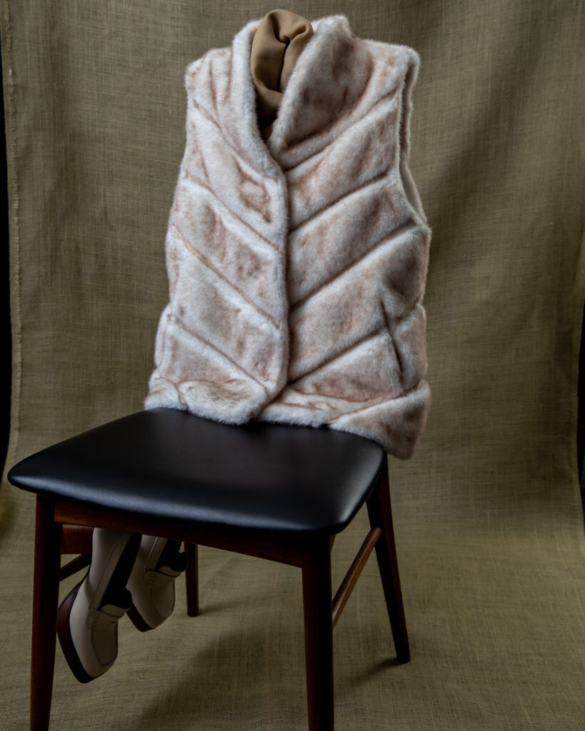 A grey fur vest sits on a black chair.