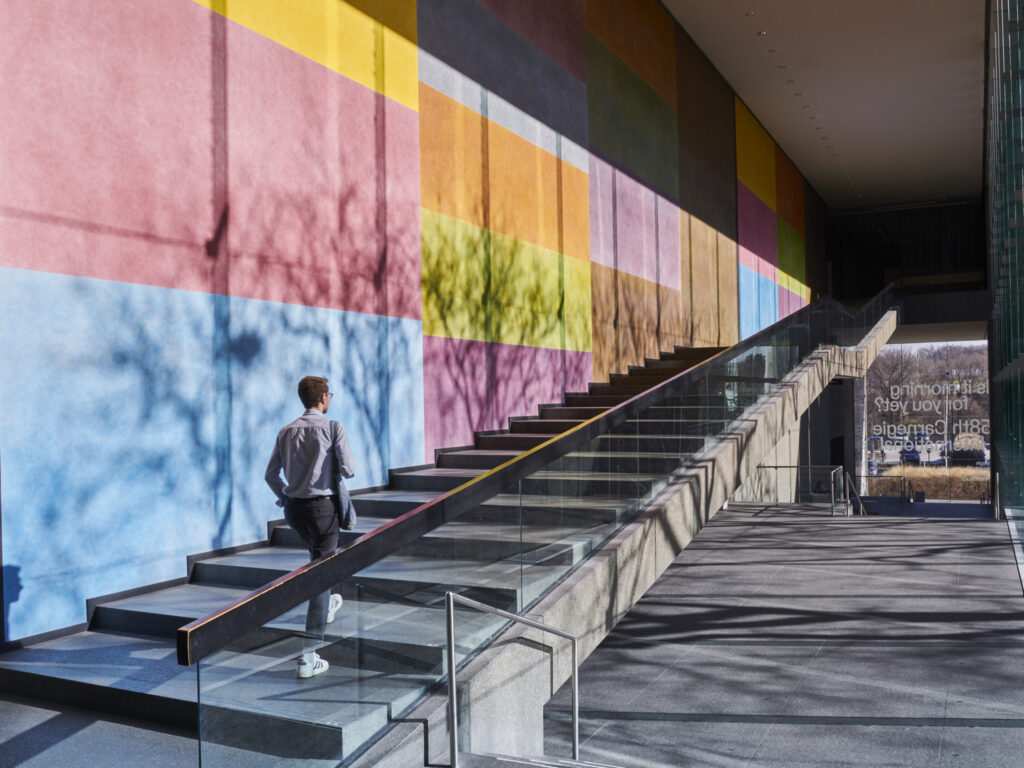 A young man walking up the steps along a painted wall outside of the Carnegie Museum of Art