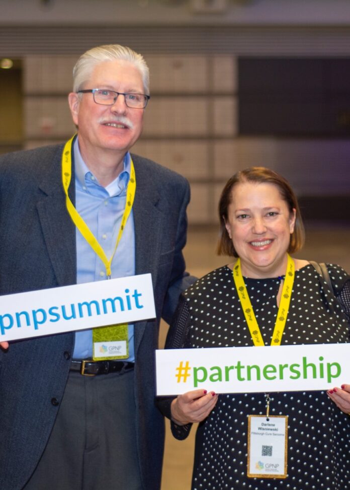 An older man and a woman hold up hashtag signs in front of their bodies.