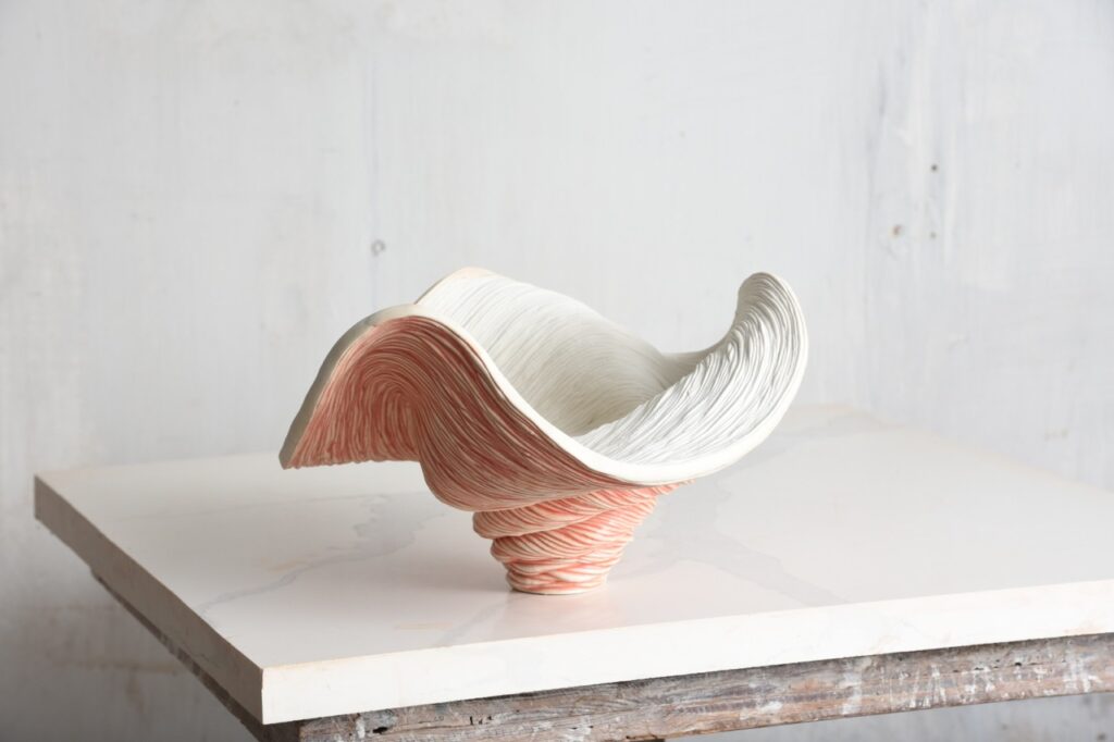 A sculpture bowl piece for home decoration has a pinkish outside and white inside in a wavy shape.