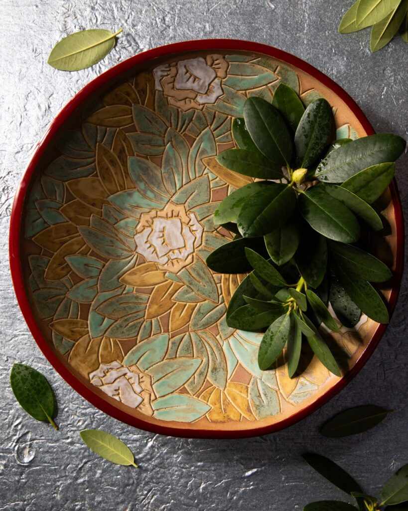 A floral green and gold bowel for the home sits with greenery placed inside.