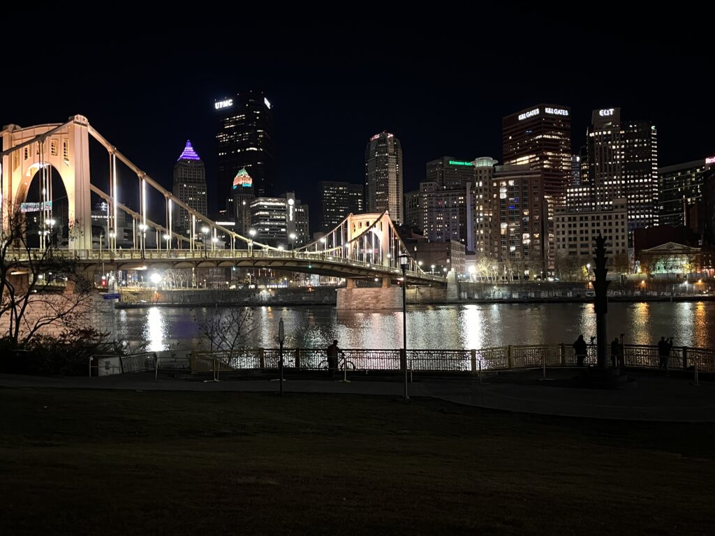 A view of a bridge lit up at night with a city behind.