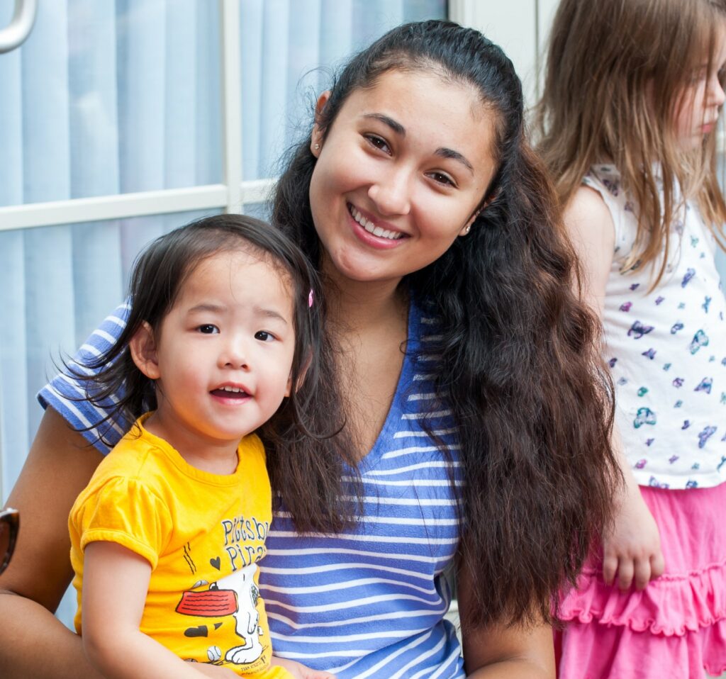 A women with l long dark hair holding a small child with a yellow shirt in her lap.