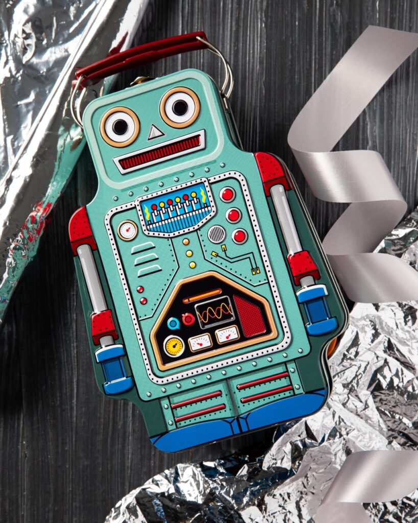 A blue robot kids toy with a handle over the head sits on a black table with silver ribbon and embellishments on the outsides of the photo.