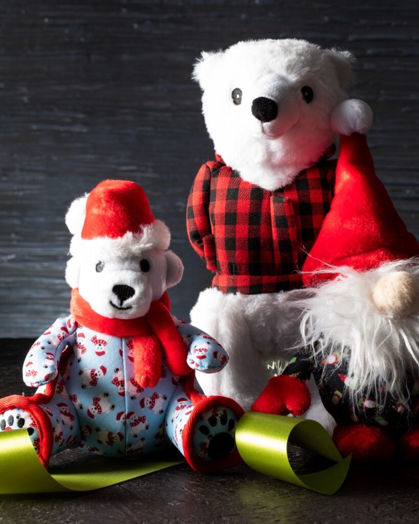 Two polar bear kids stuffed animals sit dressed in red hats, scarves, and jackets.