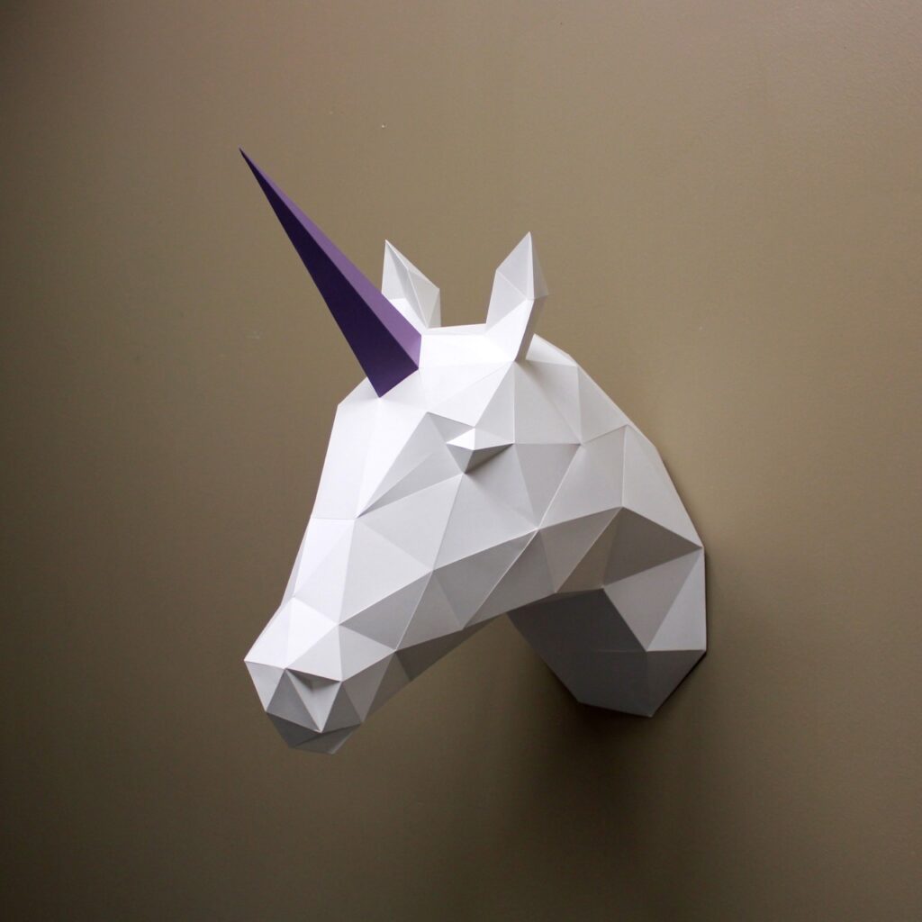 A white block shaped unicorn with a purple horn hangs off a beige wall.