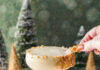 Stroopwafel Flip A creamy looking cocktail in a coupe glass with a crushed waffle cone rim on a snowy surface with cone trees and pine trees in the background.