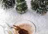 Hot, Hot, Hot, Hot Chocolate Cocktail A clear mug of hot chocolate on a snowy surface with evergreen clippings and dried ancho chili peppers.