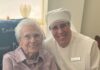 Giving Guide 2025: Little Sisters of the Poor A woman in a whit nurses outfit from the Little Sisters of the Poor holds an elderly woman's arm.