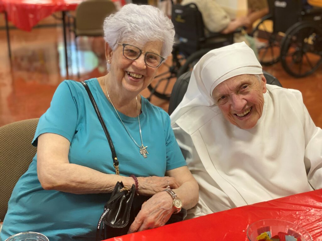 A white haired elderly women siting next to an elderly nun wearing white.